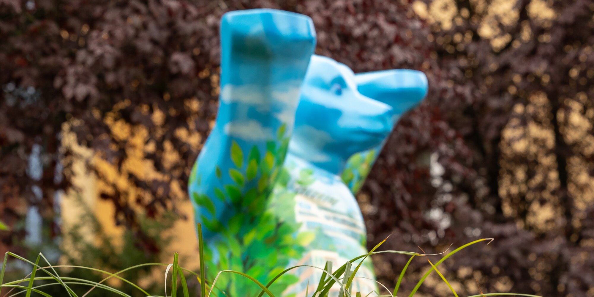 Blaue Statue in Form eines Berliner Buddy-Bären auf einer grünen Wiese.
