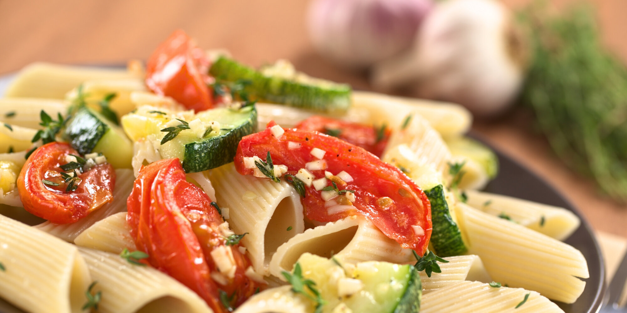 Ein Teller mit Pasta, Tomaten und Zucchini dekoriert mit frischen Kräutern.