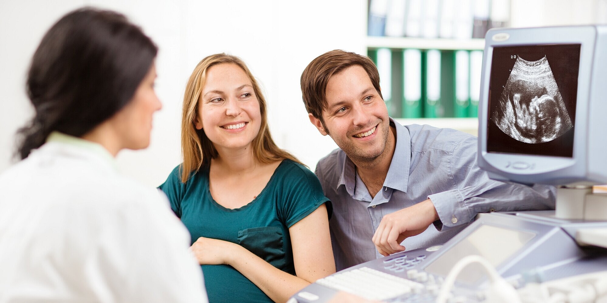 Schwangerschaft und Geburt: Rundumversorgung für werdende Eltern und Neugeborene Werdende Eltern betrachten mit Ärztin Ultraschall am Monitor.