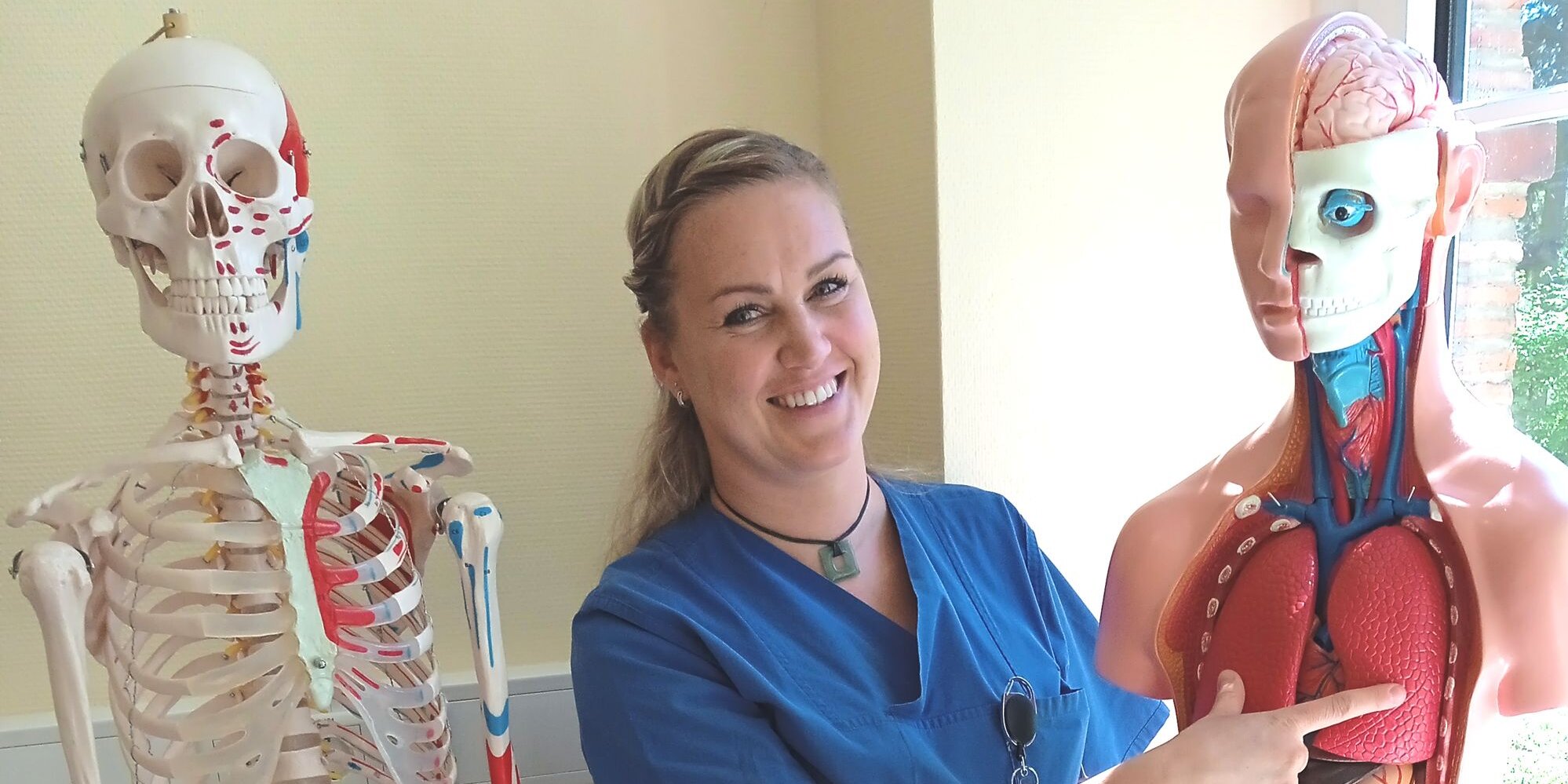 Lächelnde Pflegerin in Berufskleidung zeigt auf Lunge eines anatomischen Modells