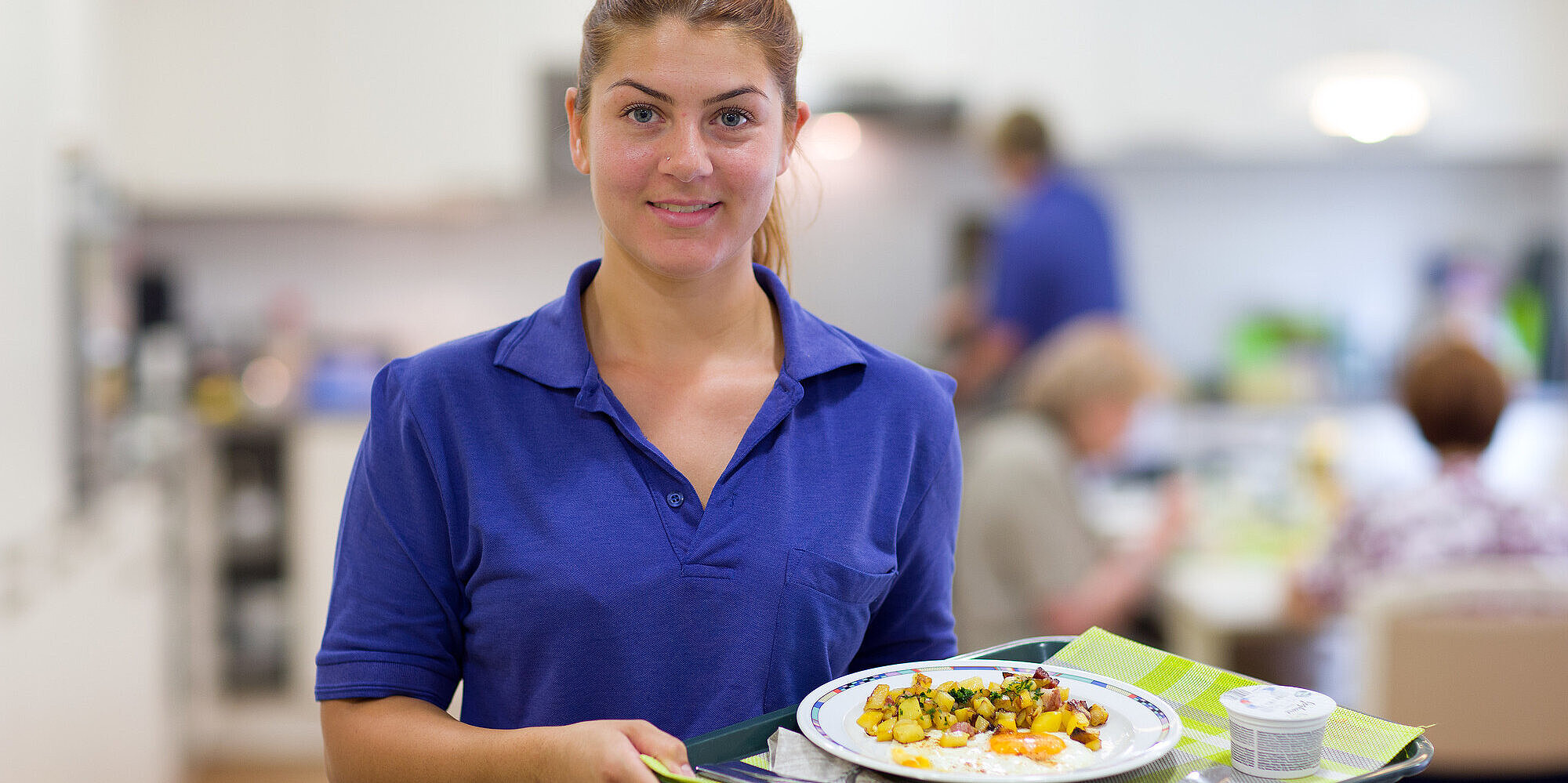 Für Ihr Frühstück, Mittag- und Abendessen halten wir eine Auswahl an verschiedenen Gerichten und Getränken bereit. Mitarbeiterin bringt Essen auf einem Tablett