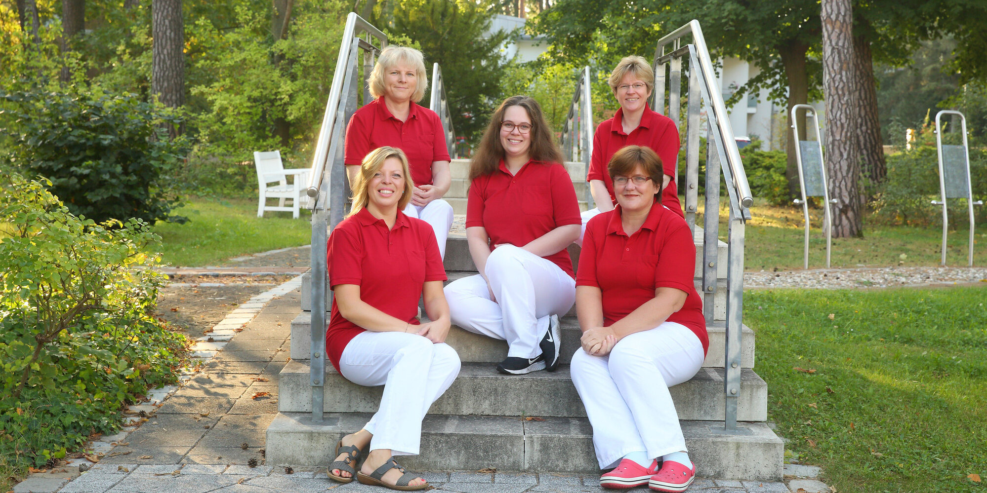 Teamfoto mit fünf Mitarbeiterinnen des Sozialdienstes, die auf einer Treppe in der Parkanlage des Evangelischen Krankenhauses Hubertus sitzen.