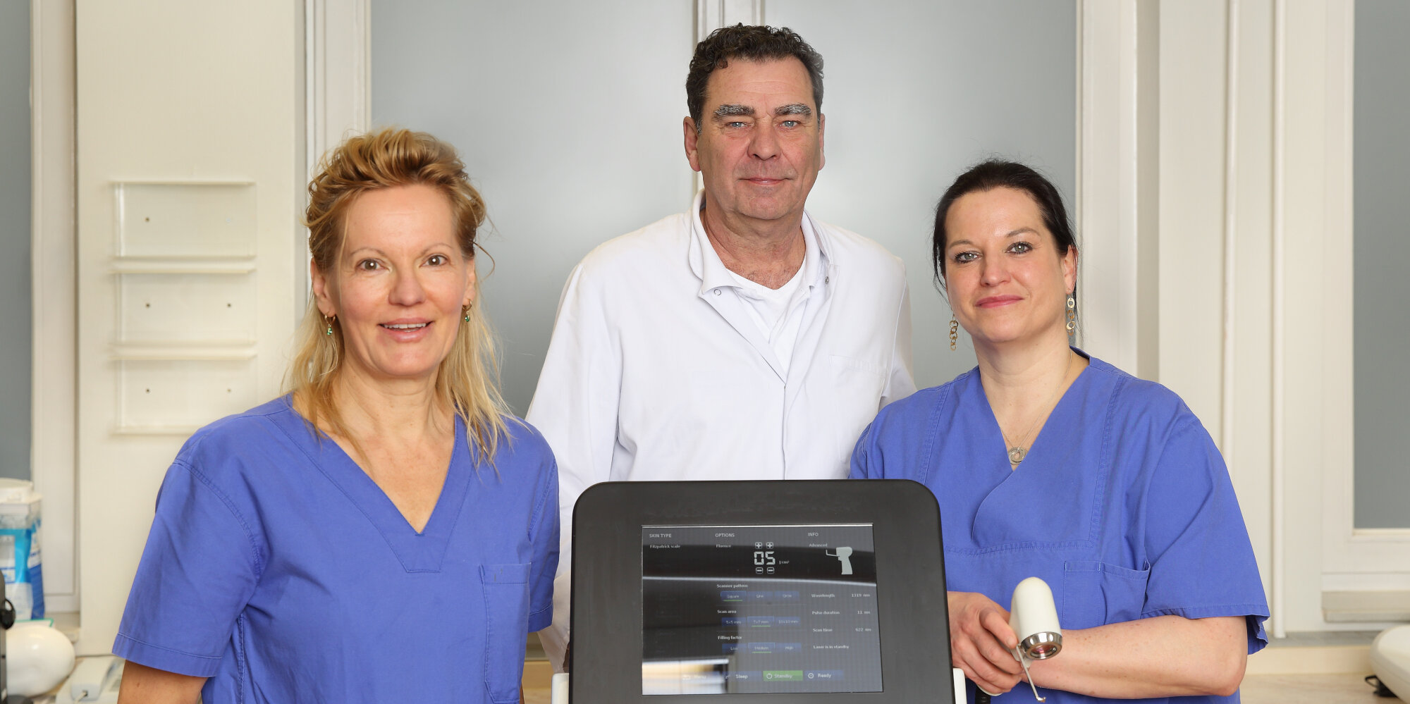 Ein Mann und zwei Frauen mit einem medizinischen Lasergerät.