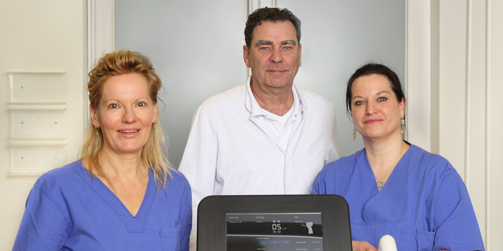 Ein Mann und zwei Frauen mit einem medizinischen Lasergerät.