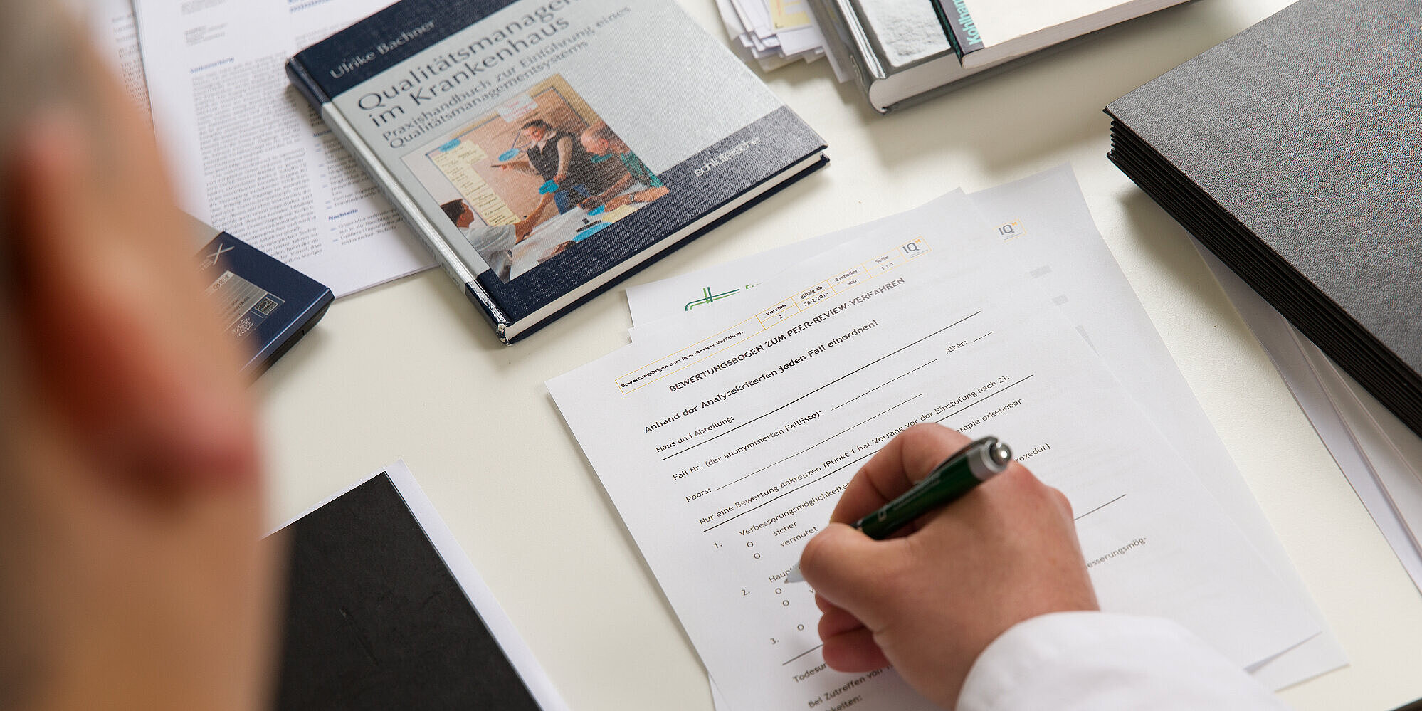 Qualitätsmanagement: Mehr Sicherheit und Zufriedenheit für Patient*innen und Bewohner*innen Mitarbeiter füllt einen auf dem Tisch liegenden Fragebogen aus.