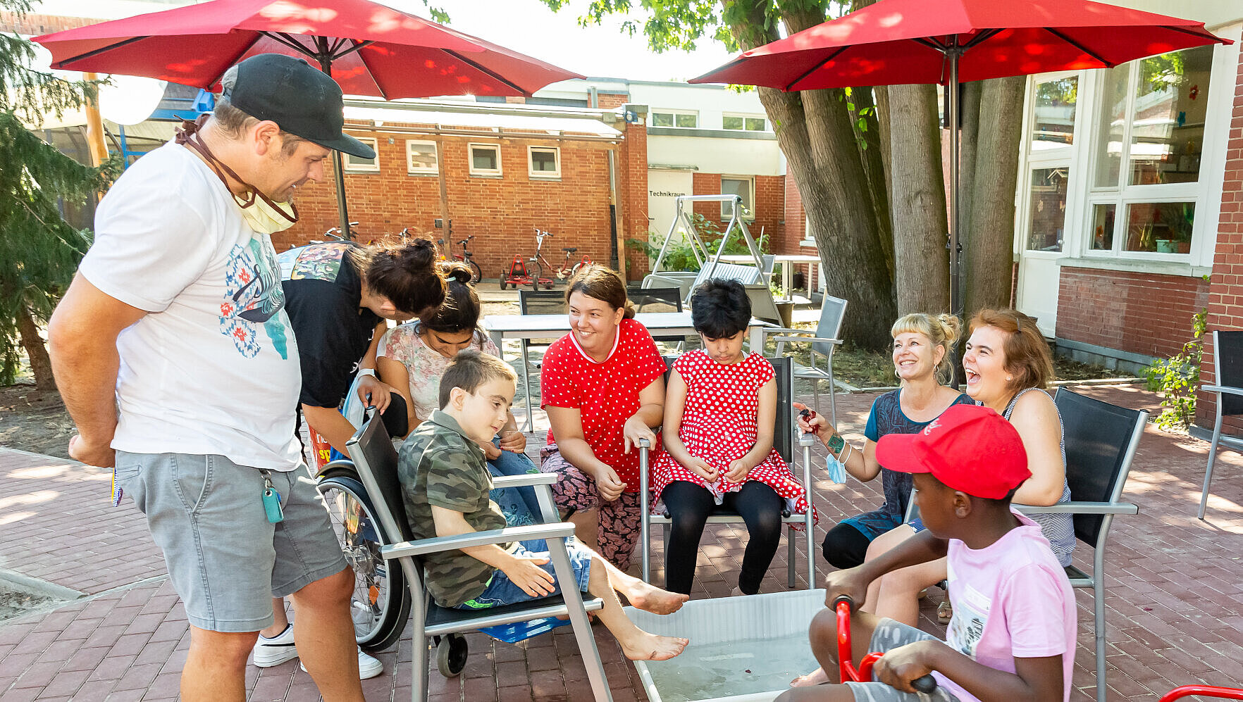 Hort: Ergänzende Förderung und Betreuung Hortkinder und deren Betreuer*innen sitzen draußen in einem Stuhlkreis. In der Mitte steht eine mit Wasser gefüllte Wanne für ein Fußbad.