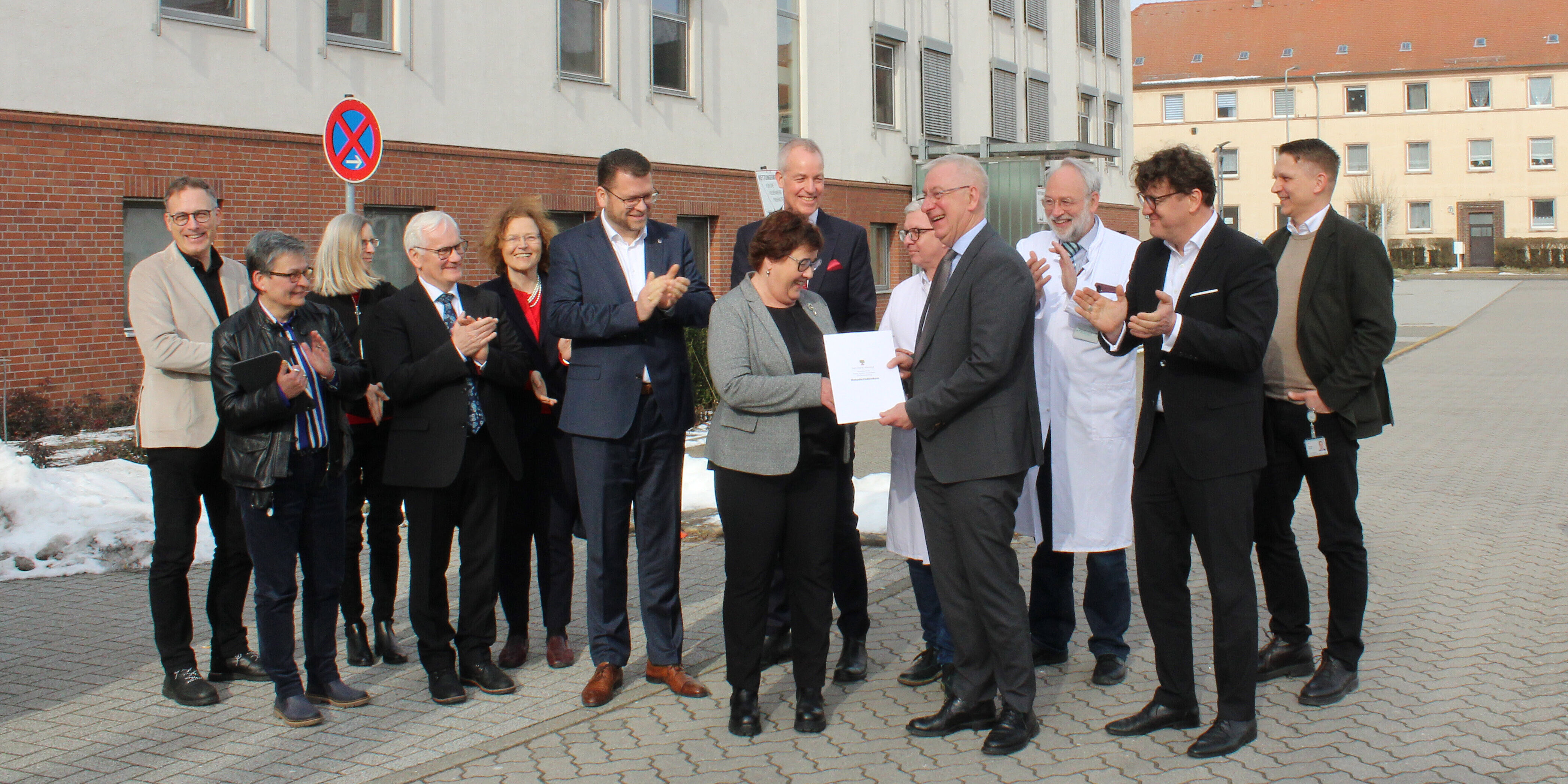 Gruppenbild von Mitarbeitenden des Klinikums, ganz vorne übergibt die Gesundheitsministerin Unterlagen an den Geschäftsführer.