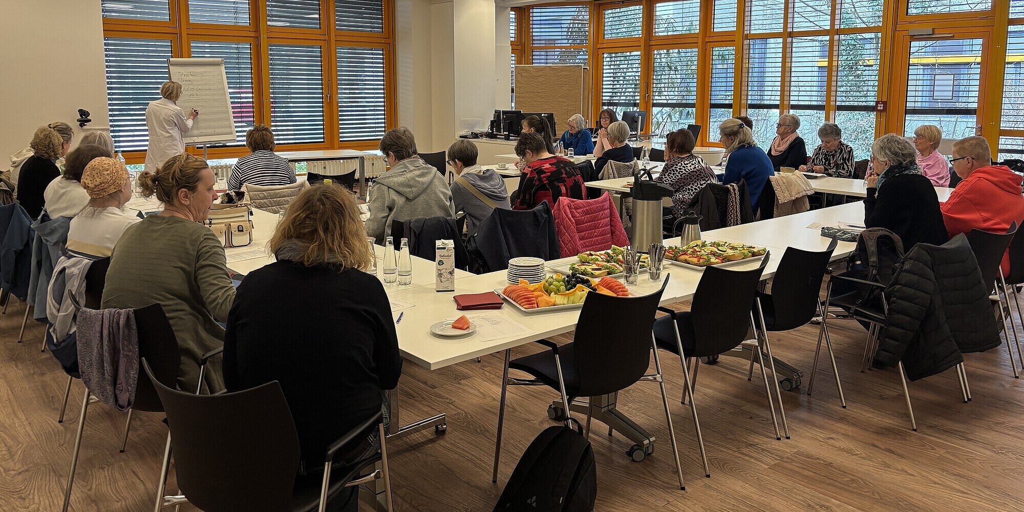 Ein zentrales Anliegen der Veranstaltung war es, den Patientinnen Informationen an die Hand zu geben, die ihnen helfen, ihre Nachsorge und den Umgang mit Metastasen besser zu verstehen und aktiv mitzugestalten. Besucher*innen sitzen an Tischen im Patientenzentrum des Evangelischen Waldkrankenhauses Spandau