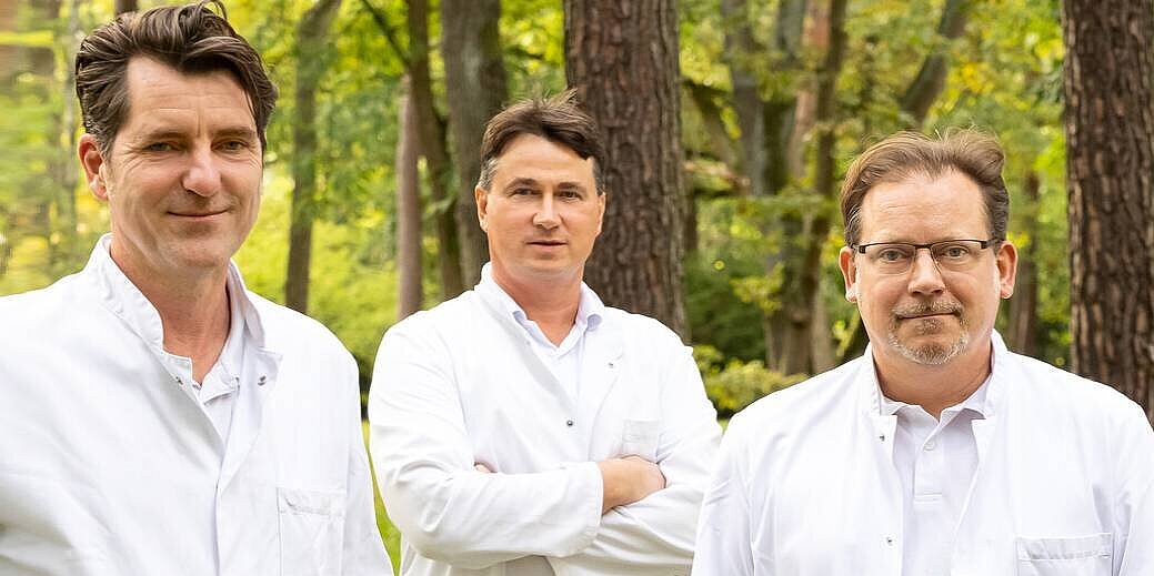Drei Ärzte der Wirbelsäulenchirurgie im Arztkittel stehen nebeneinander.