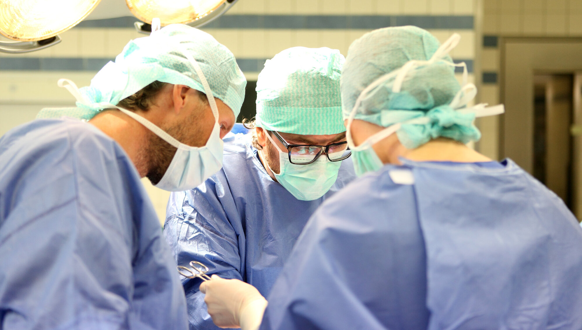 Drei Ärzte in OP-Kleidung operieren einen Patienten.