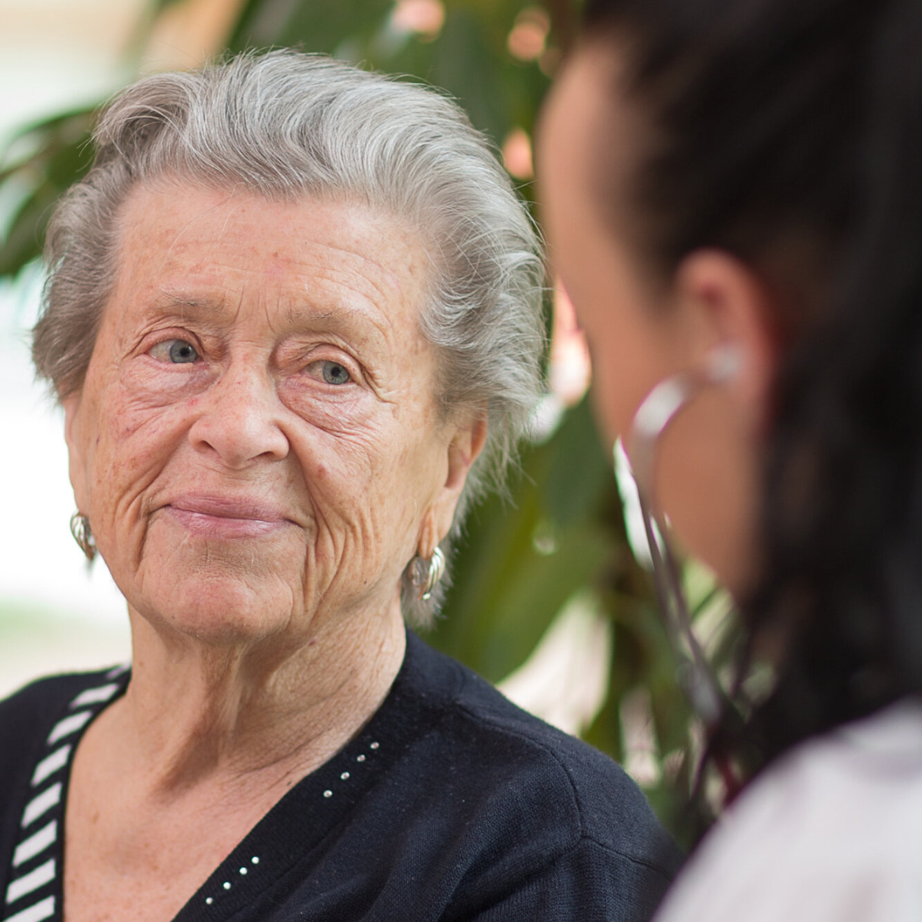 Eine Pflegekraft mit Stethoskop untersucht eine ältere Frau.