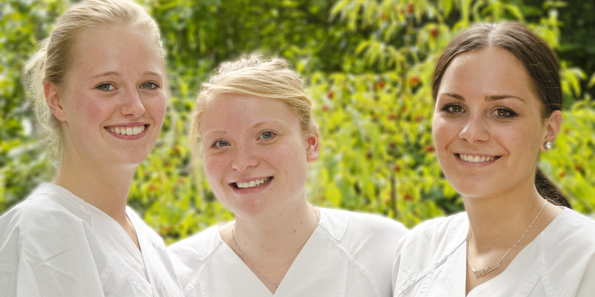Drei Auszubildende der Pflege stehen nebeneinander und lächeln.
