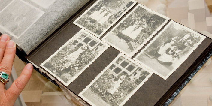 Seite aus einem Fotoalbum mit alten Schwarz-Weiß-Fotoaufnahmen, auf denen Frauen in einem Garten abgebildet sind.