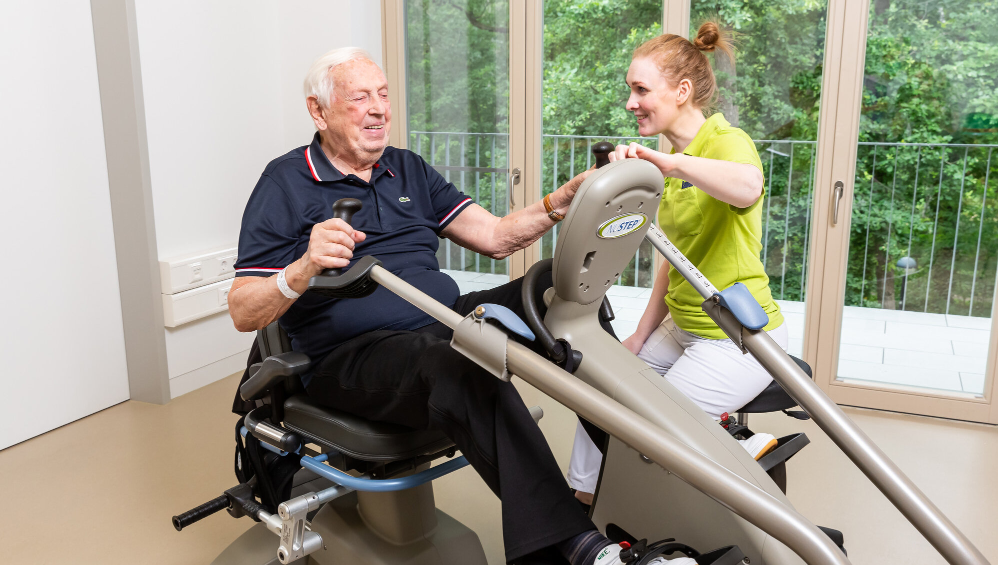 Älterer Patient trainiert mit Ergotherapeutin an einem Sportgerät.