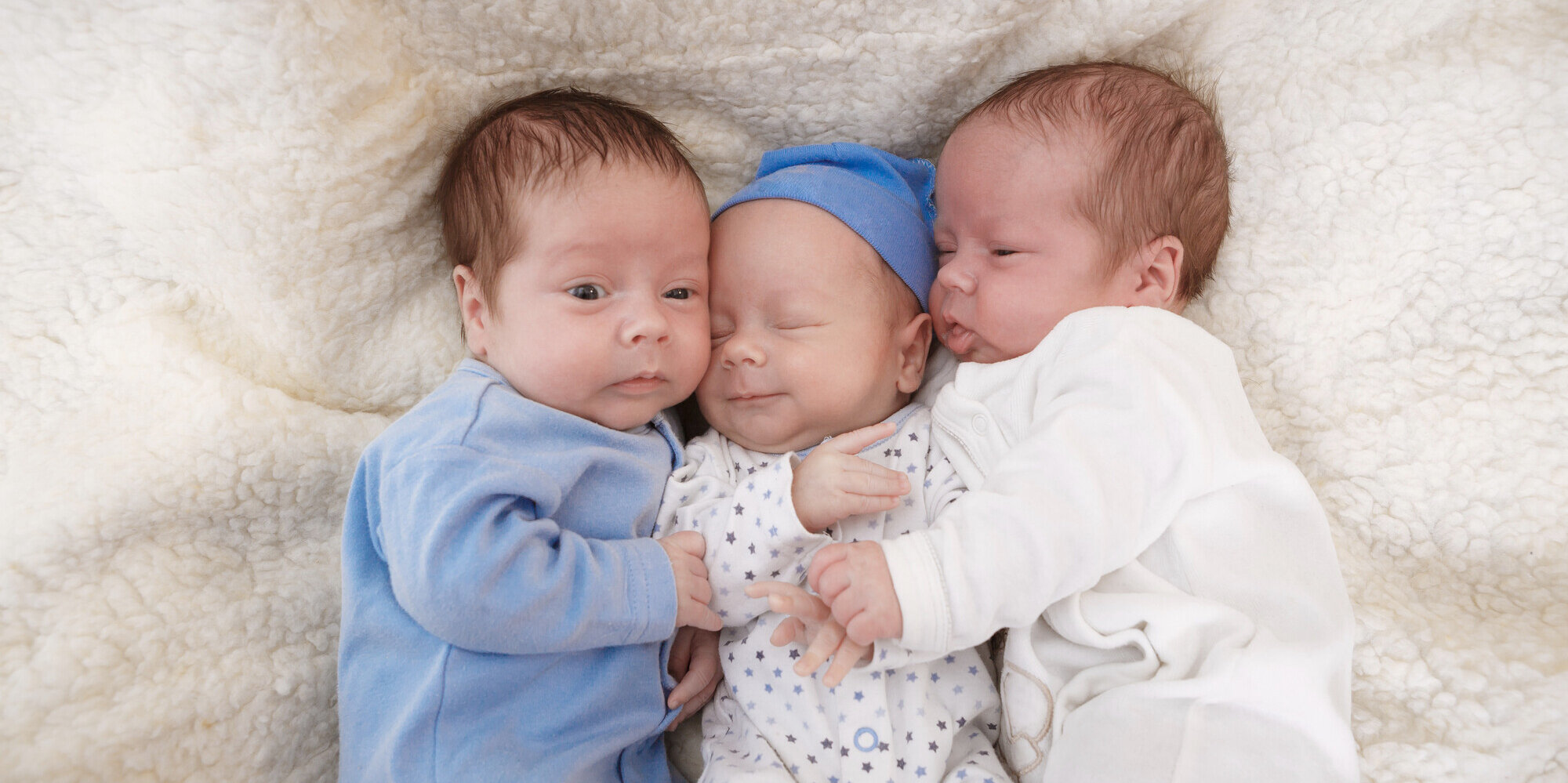 Drei neugeborene Babies liegen auf einer Decke.