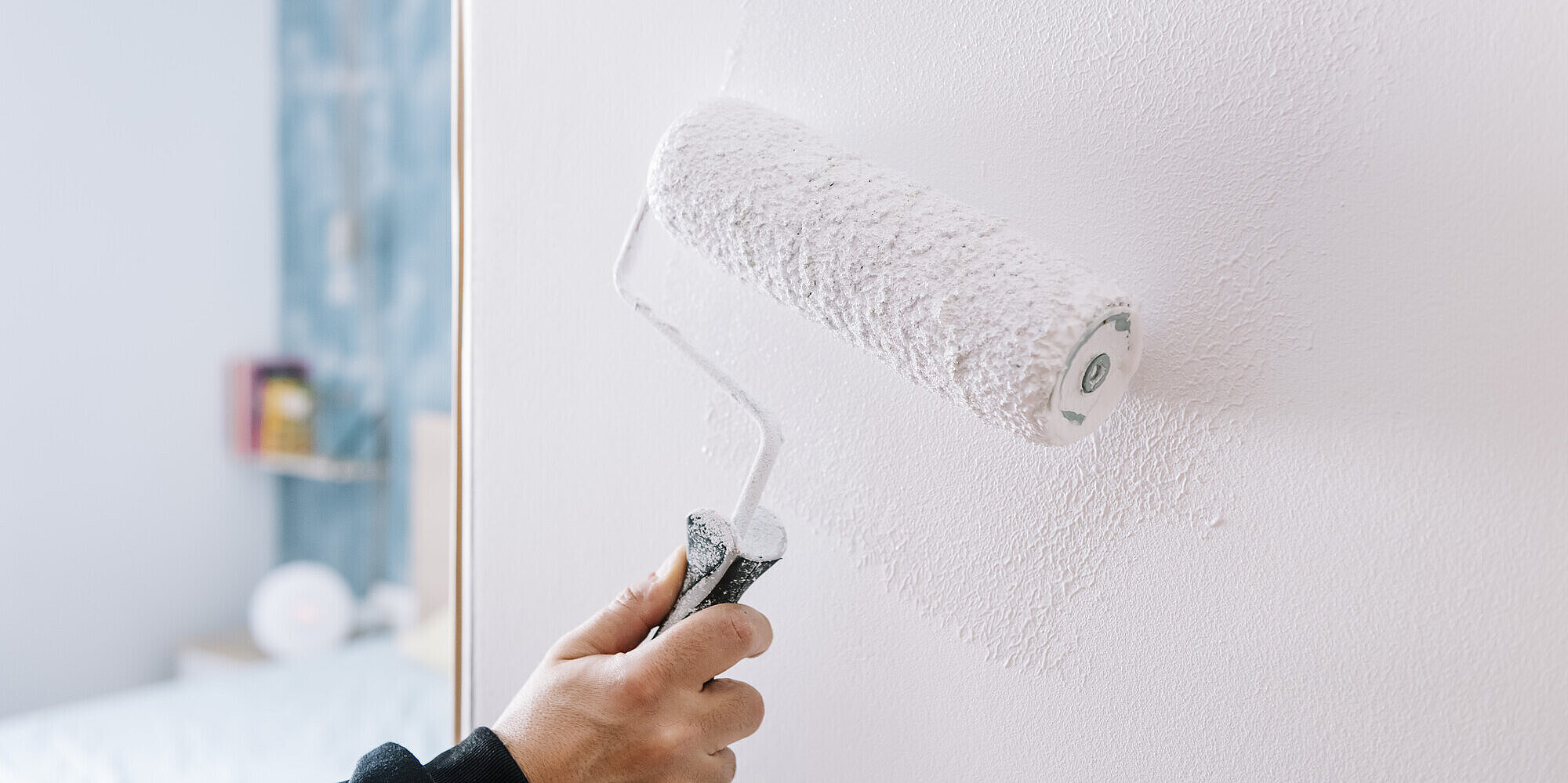 Malerarbeiten für Geschäfts- & Privatkund*innen Symbolbild Malereibetrieb mit Detailaufnahme einer Malerrolle, die eine weiße Wand streicht