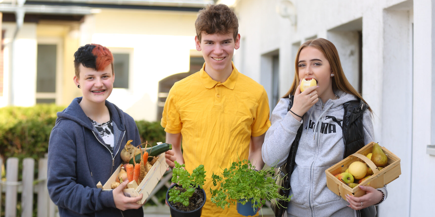 Drei Jugendliche mit Obst- und Gemüsekisten in den Händen.