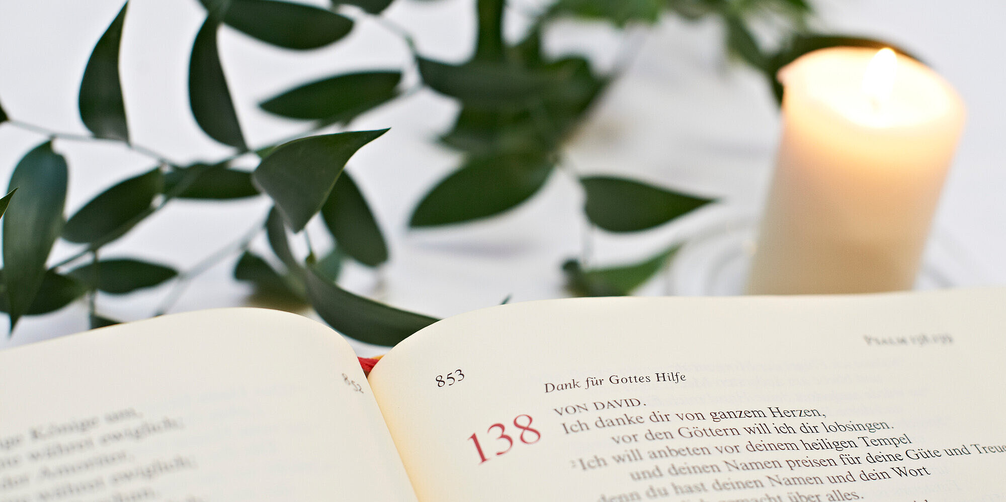 Eine aufgeschlagene Bibel mit einem Psalm und daneben eine brennende Kerze.