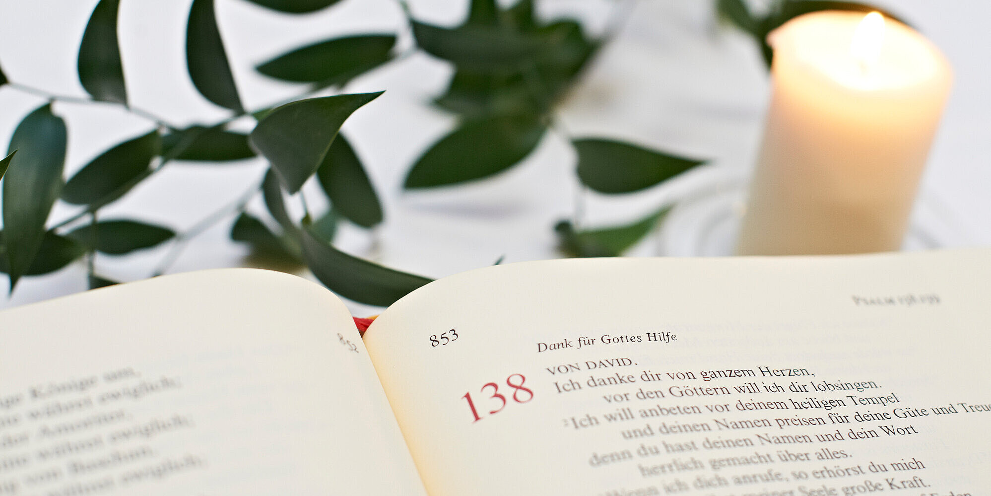 Eine aufgeschlagene Bibel mit einem Psalm und daneben eine brennende Kerze.