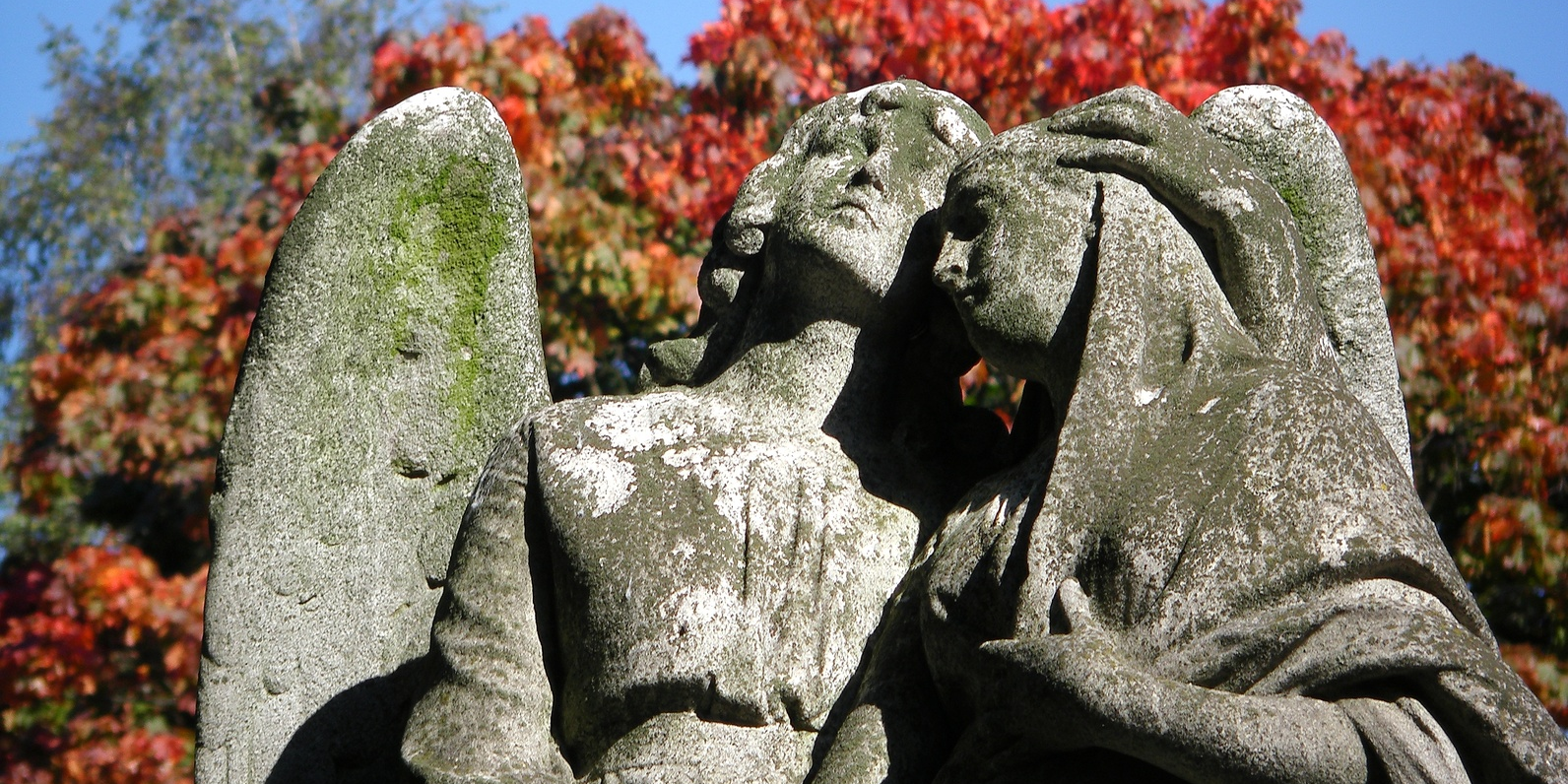 Zwei große Engel-Statuen aus Stein stehen nebeneinander und haben die Köpfe aneinander gelehnt.