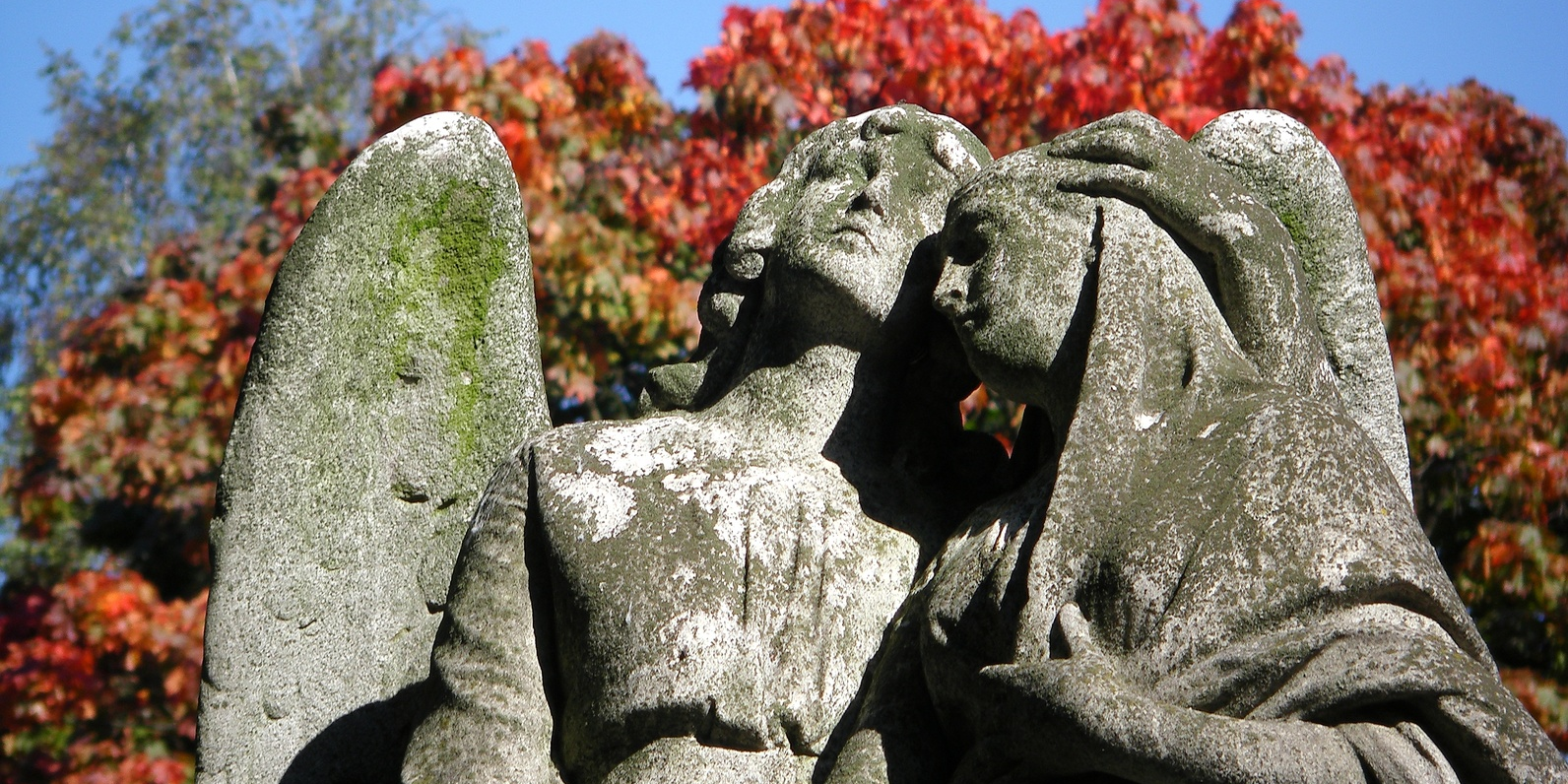 Zwei große Engel-Statuen aus Stein stehen nebeneinander und haben die Köpfe aneinander gelehnt.
