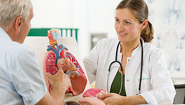 Junge Ärztin erklärt einem Patienten etwas an einem Lungenmodell.