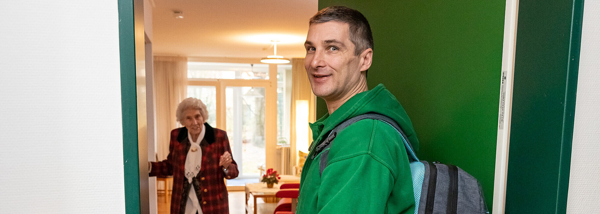 Professionelle und zugewandte Pflege und Betreuung in Ihrem Zuhause Ein Pfleger besucht eine ältere Dame zuhause. Sie macht ihm die Tür.