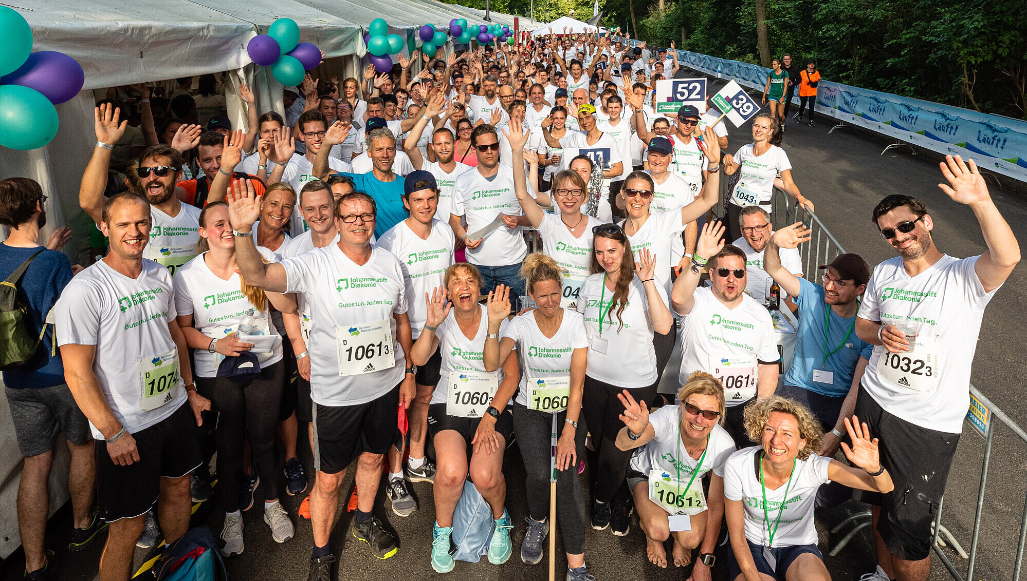 Viele Mitarbeiterinnen und Mitarbeiter mit Laufshirt stehen eng nebeneinander und freuen sich auf den Staffellauf.