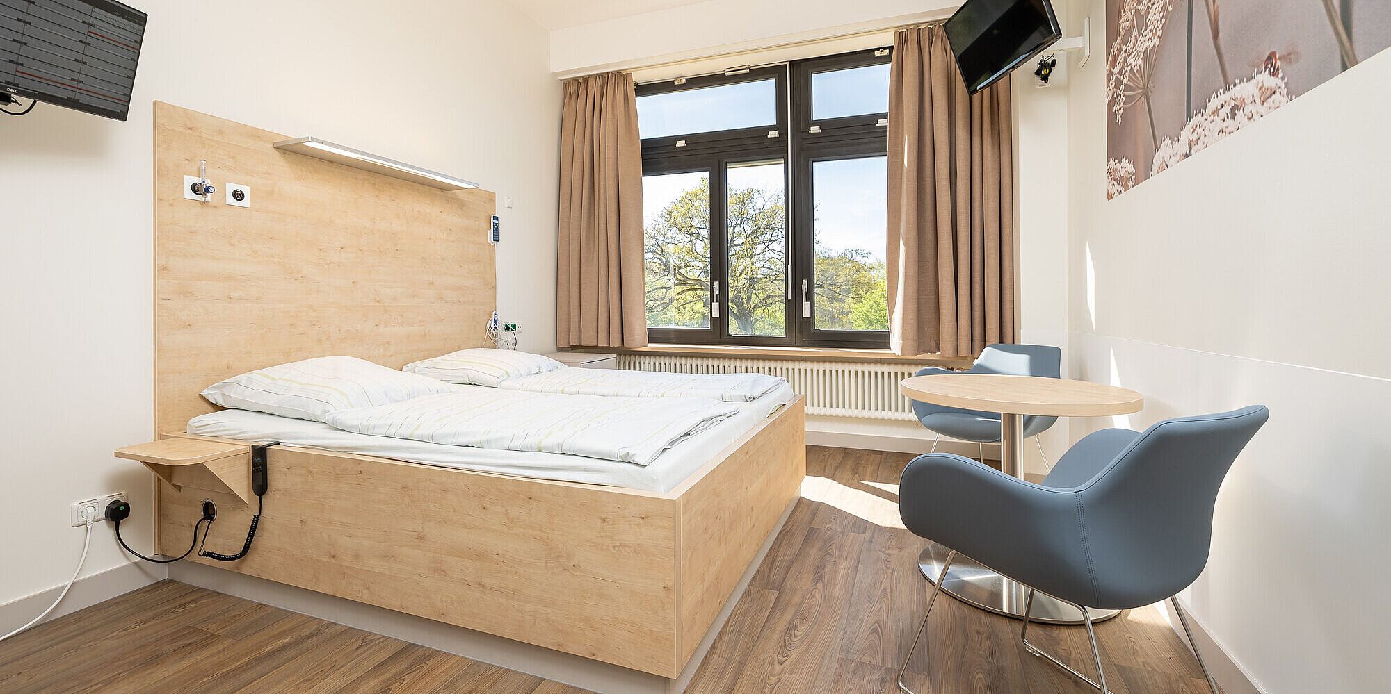Lichtdurchflutetes Zimmer mit Doppelbett, Tisch und zwei Stühlen.
