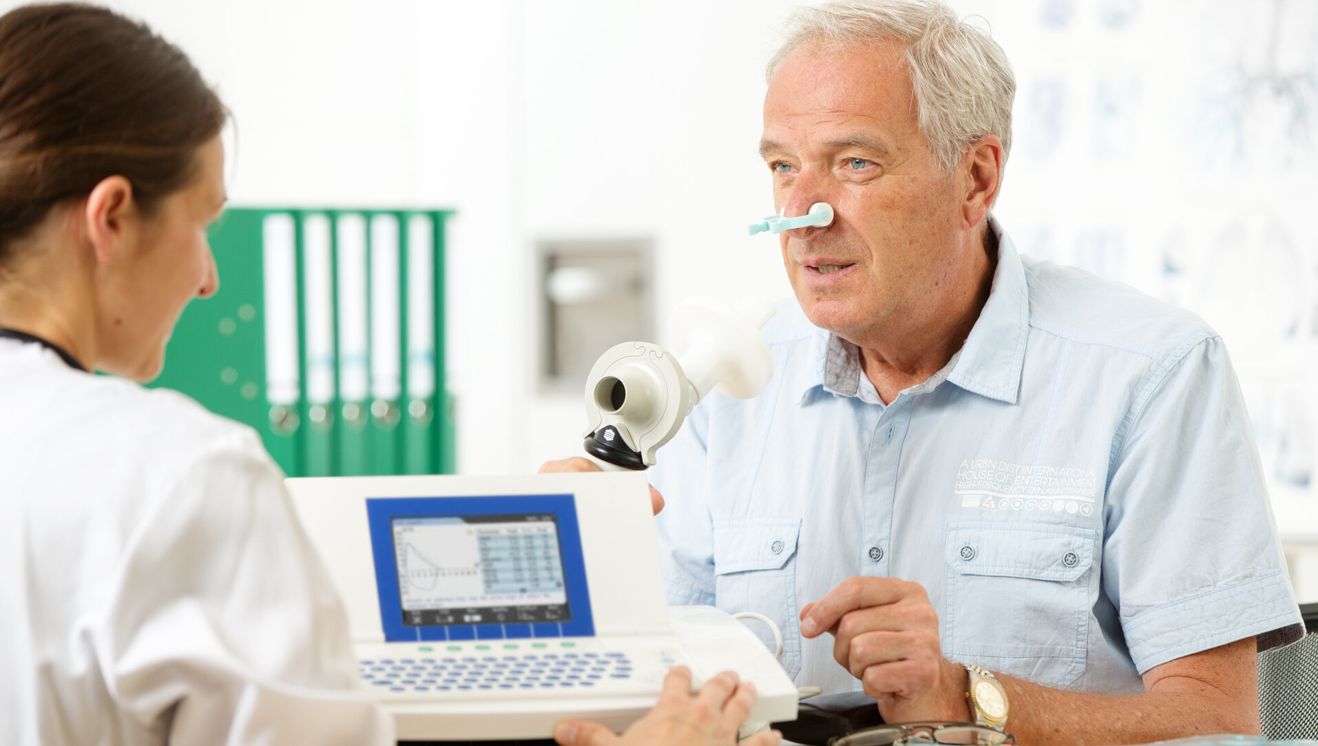 Eine Ärztin leitet einen älteren Patienten bei der Durchführung eines Lungenfunktionstests an.
