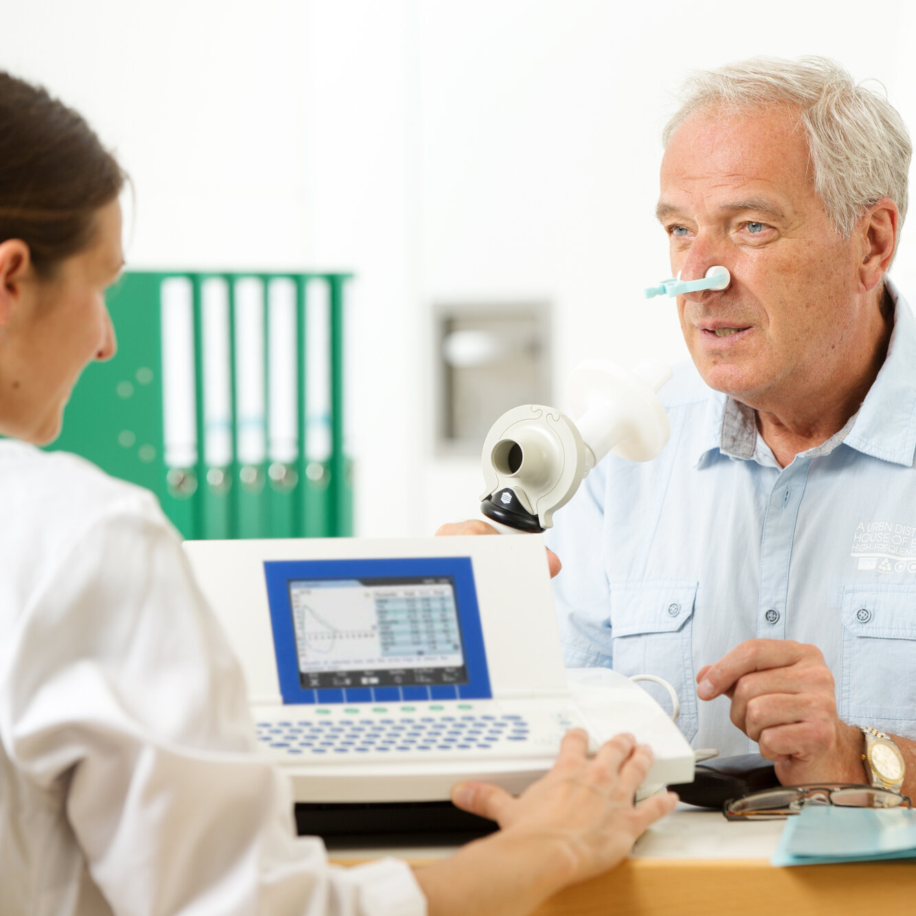 Eine Ärztin leitet einen älteren Patienten bei der Durchführung eines Lungenfunktionstests an.