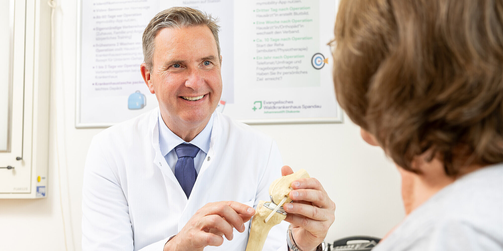 Prof. Dr. med. habil. Ulrich Nöth MHBA, Klinikdirektor der Klinik für Orthopädie und Unfallchirurgie, zeigt einer Patientin ein künstliches Kniegelenk.