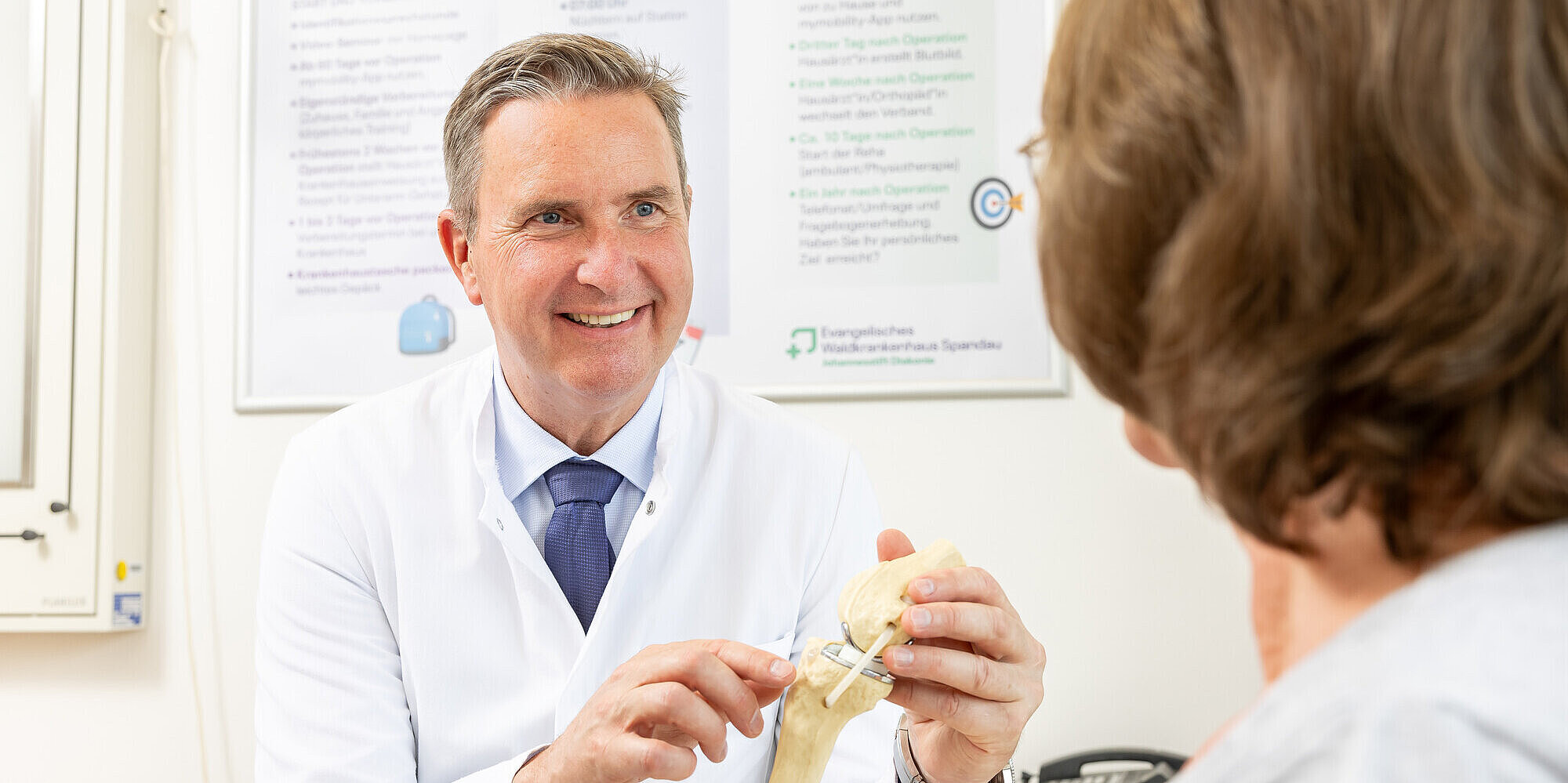 Prof. Dr. med. habil. Ulrich Nöth MHBA, Klinikdirektor der Klinik für Orthopädie und Unfallchirurgie, zeigt einer Patientin ein künstliches Kniegelenk.
