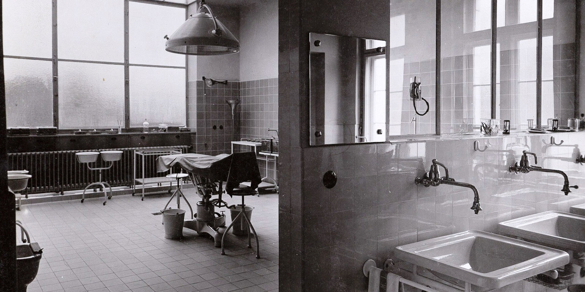 Schwarz-weiß Aufnahme eines früheren OP-Saals mit Handwaschbecken und weiterer OP-Ausstattung.