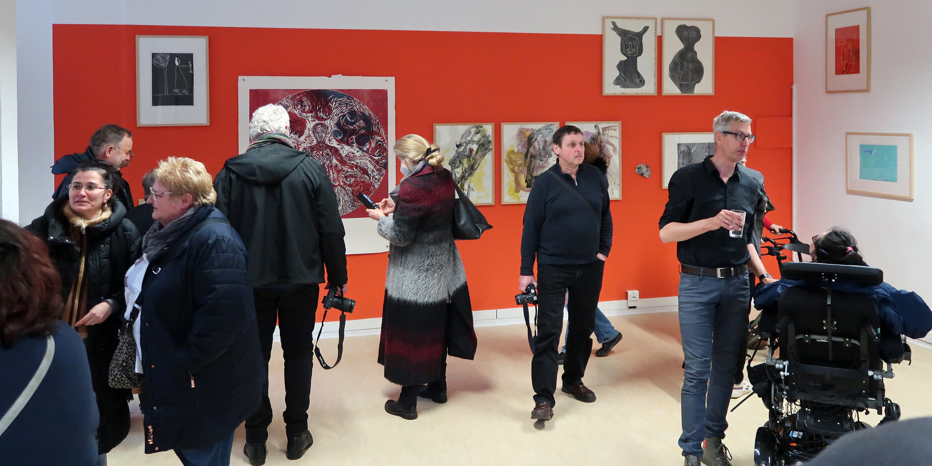 Viele Personen in einem Raum vor einer roten Wand mit Ausstellungsstücken