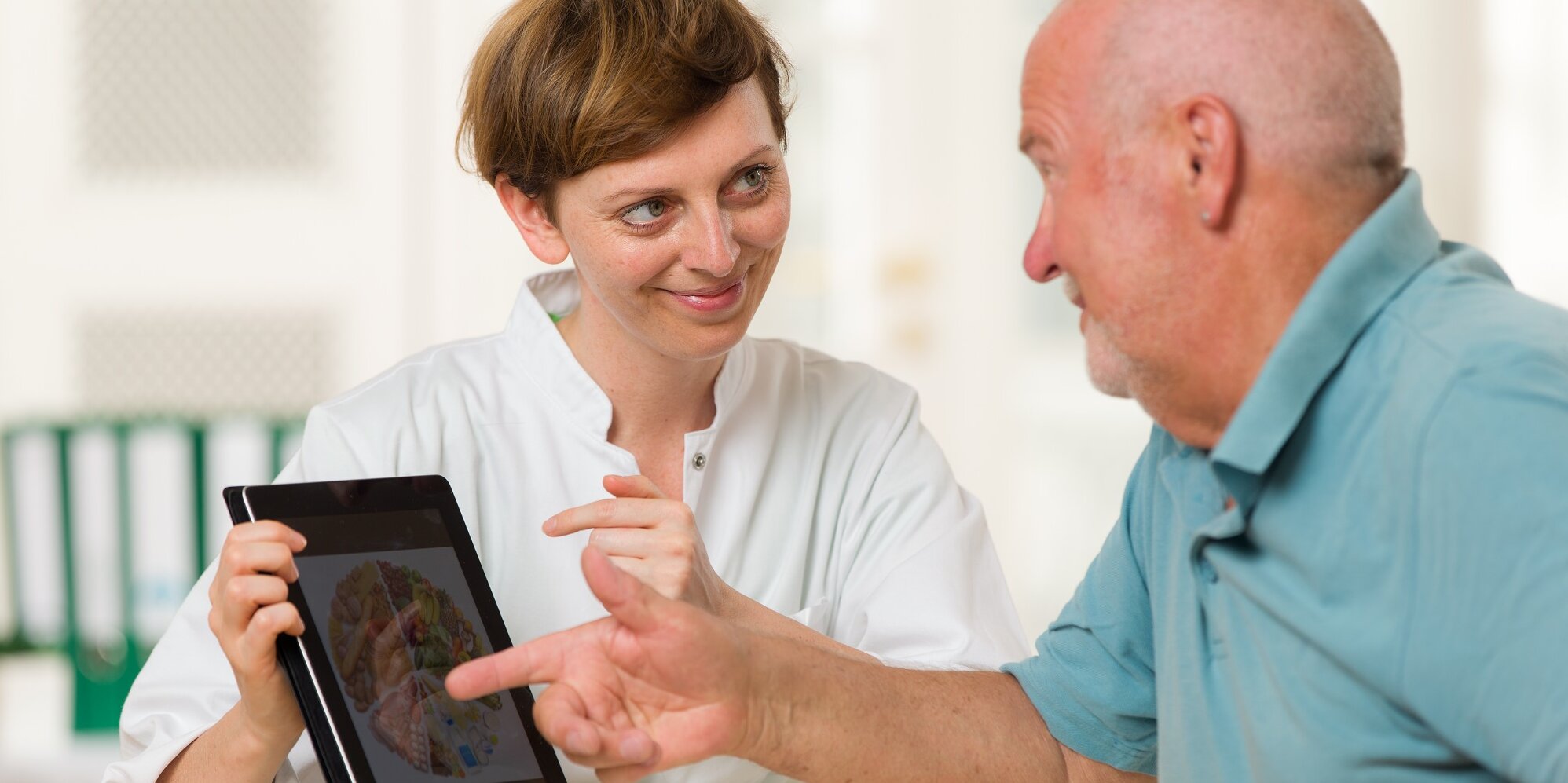 Eine junge Ärztin berät einen älteren Patienten mit einem Tablet.