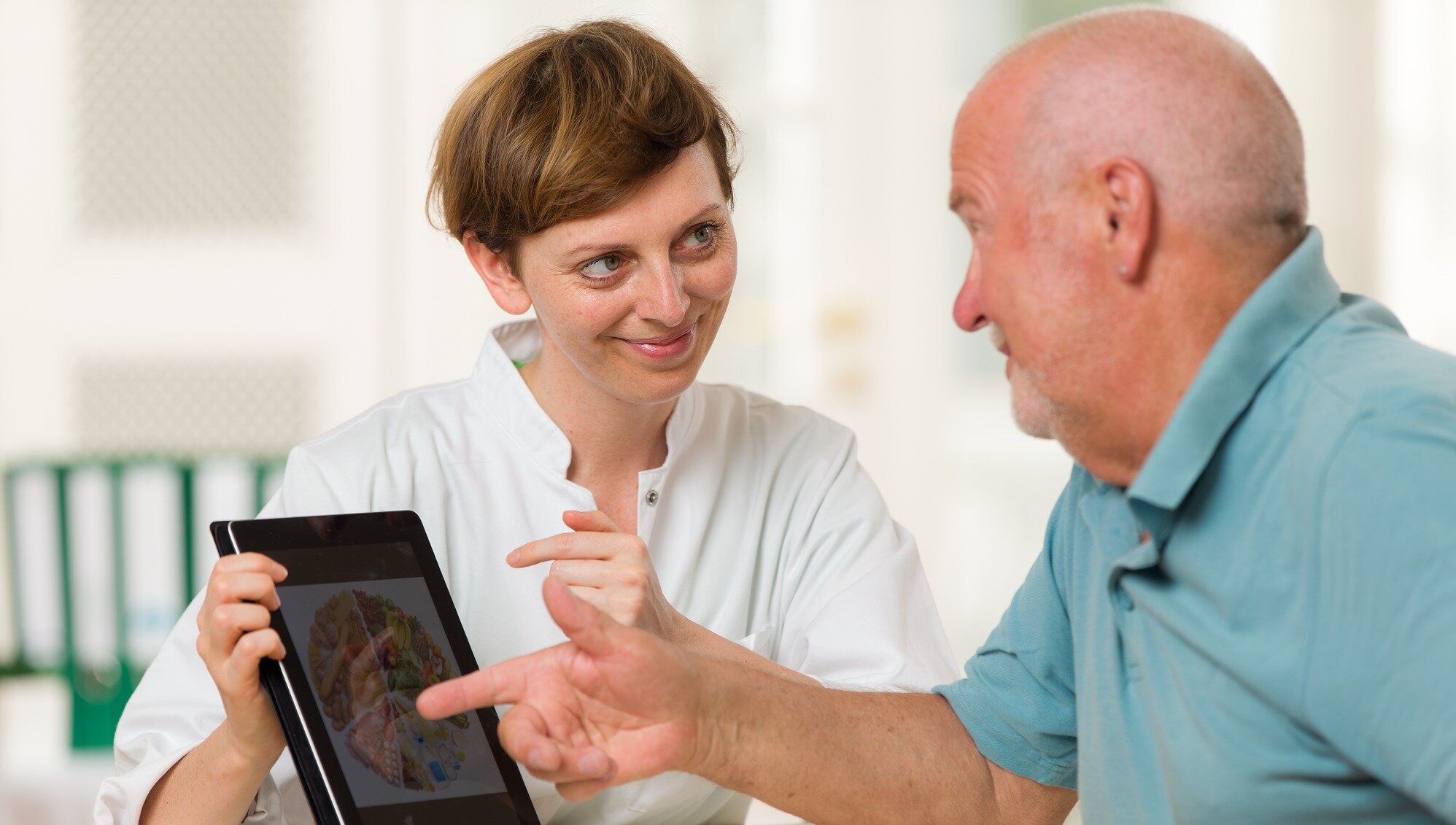 Eine junge Ärztin berät einen älteren Patienten mit einem Tablet.