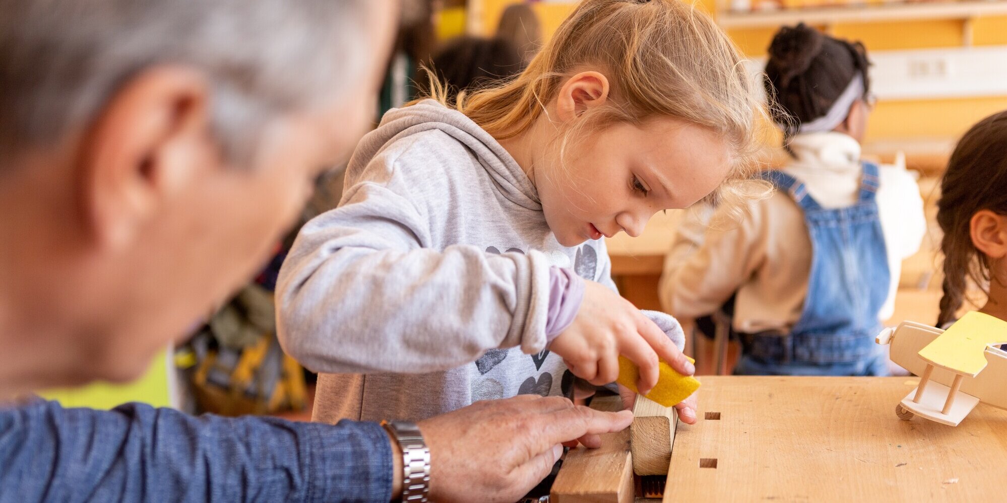 Mädchen schleift Holzstück mit Hilfe eines Erwachsenen