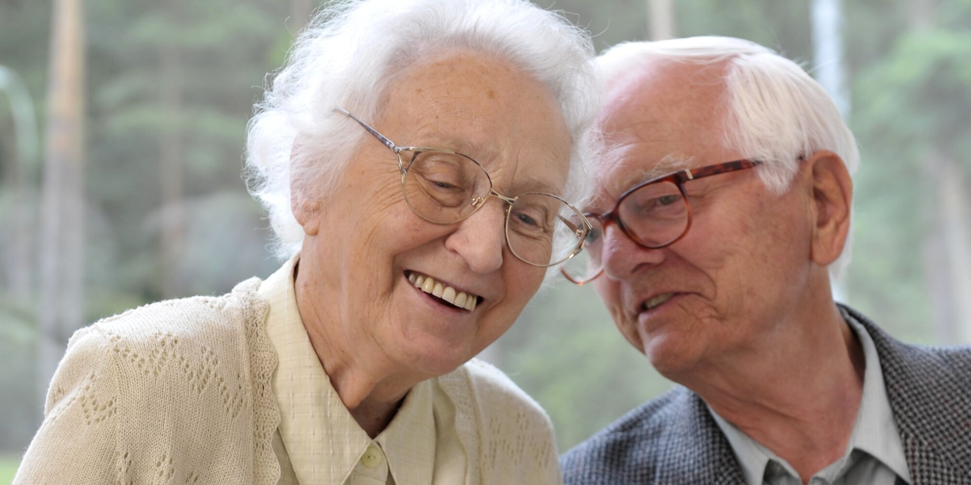 Zwei alte Menschen mit Brille sitzen fröhlich nebeneinander.