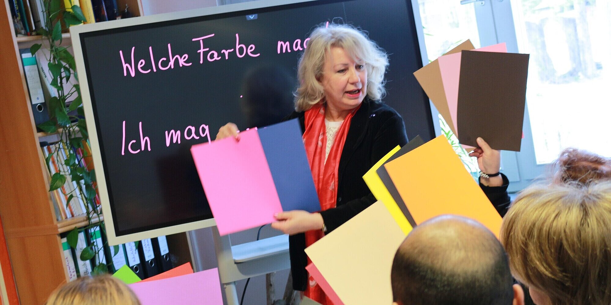 Frau steht vor Schulklasse mit bunten Blättern.