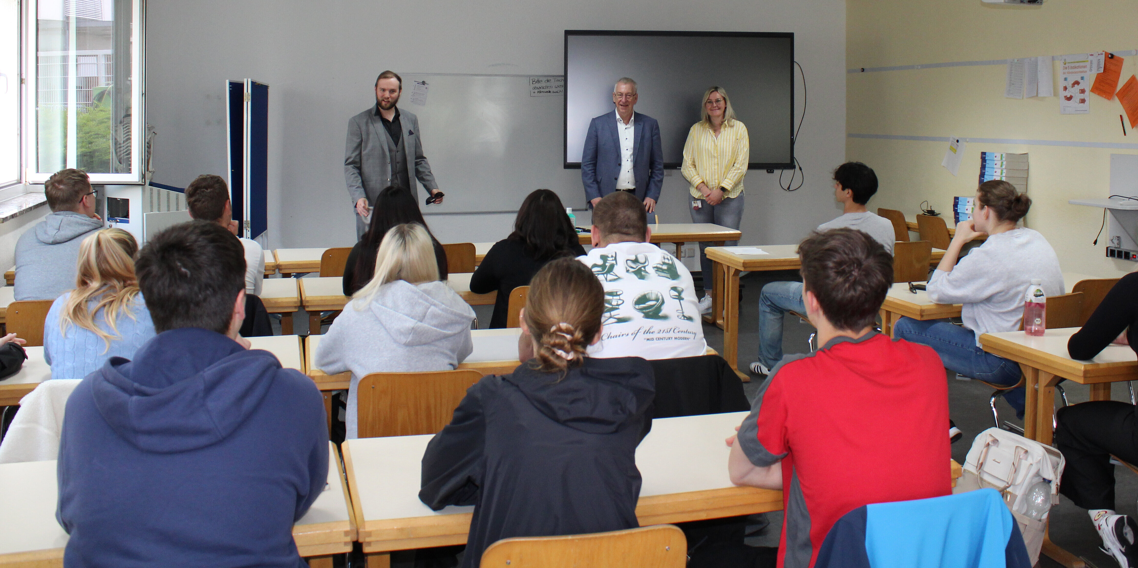 Azubis bekommen Arbeitsverträge im Klassenzimmer überreicht