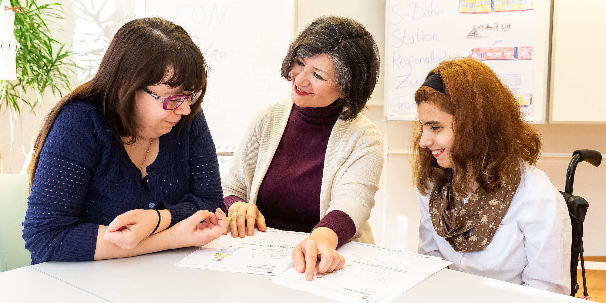 Drei Frauen arbeiten mit Arbeitsblättern an einem Tisch.