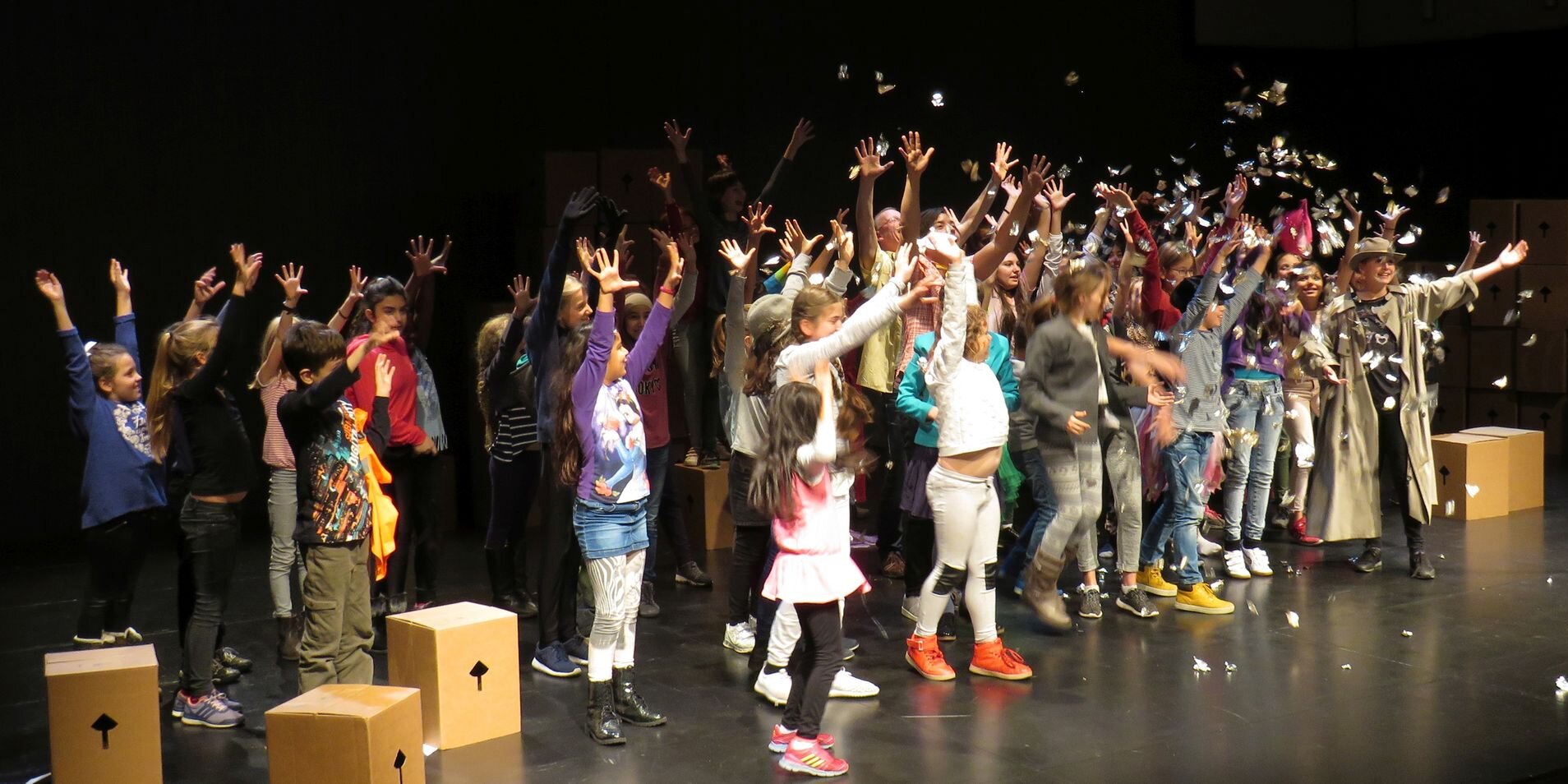 Kinder werfen auf einer Bühne Konfetti und strecken ihre Hände in die Höhe.