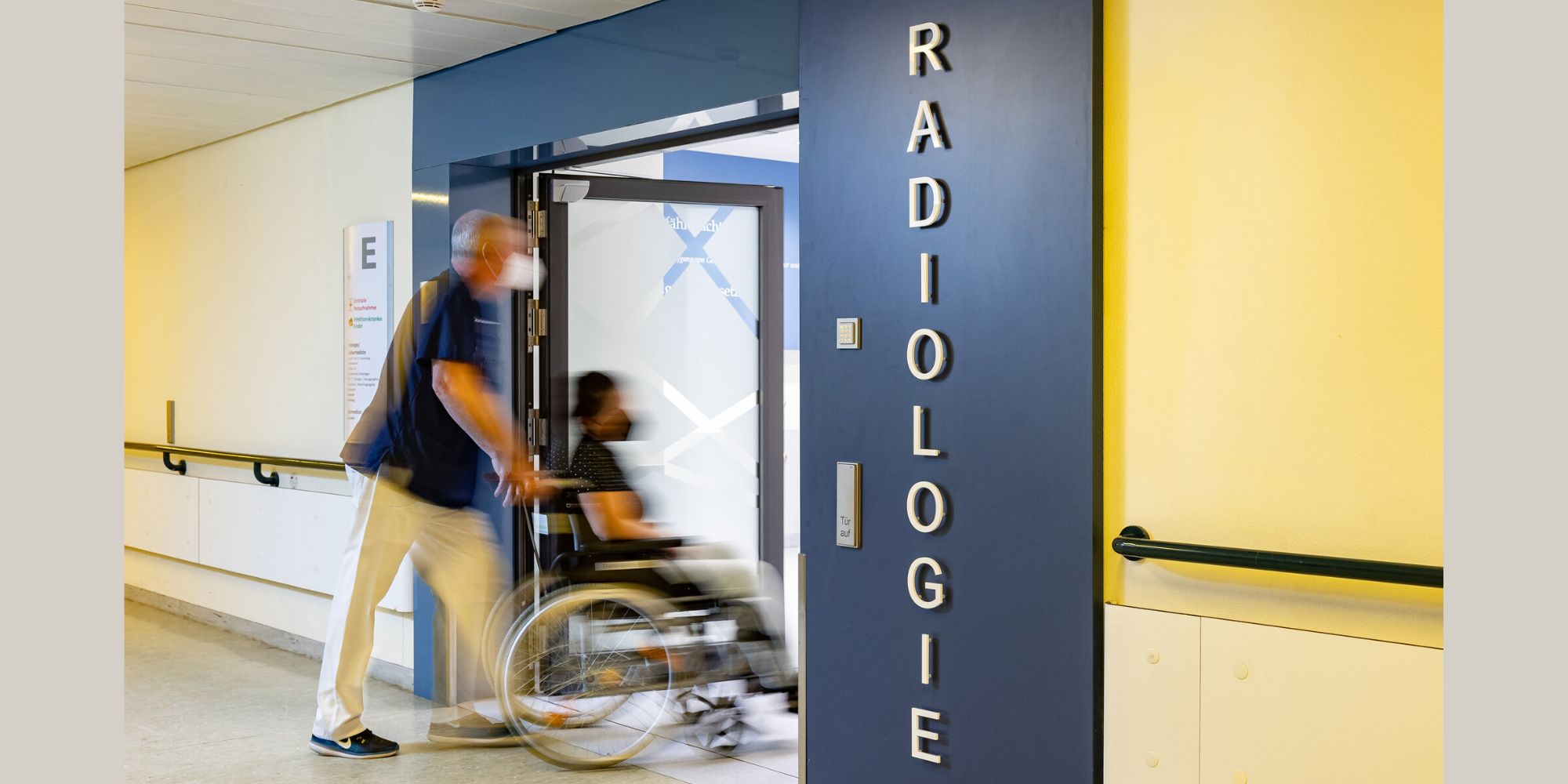 Pfleger schiebt Mann im Rollstuhl durch den Eingang der Radiologie