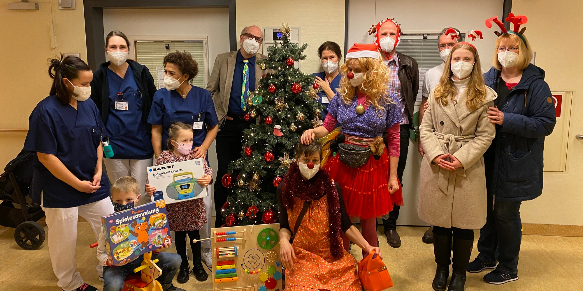 Erwachsene und Kinder stehen vor einem Weihnachtsbaum mit Geschenken.