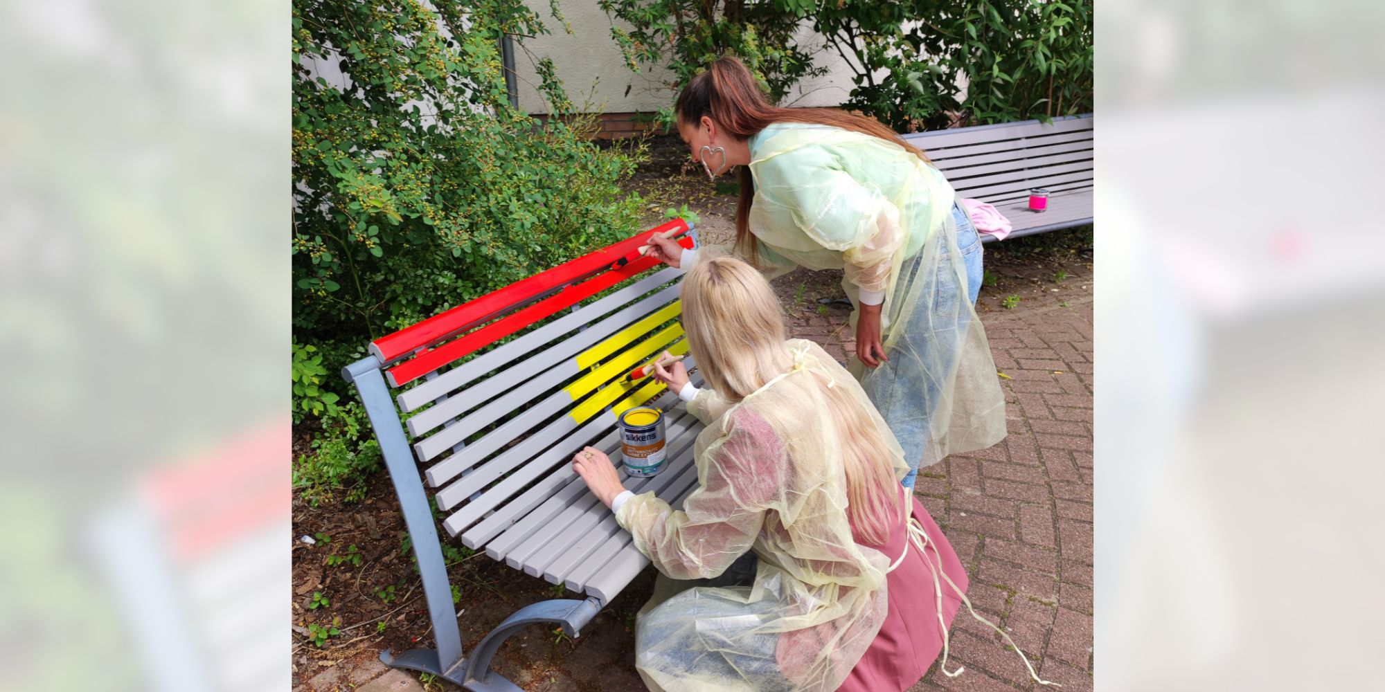 Wir sind bunt, sagt das Team mit den gestalteten Bänken. Mitarbeitende bemalen eine Bank mit Farbe.