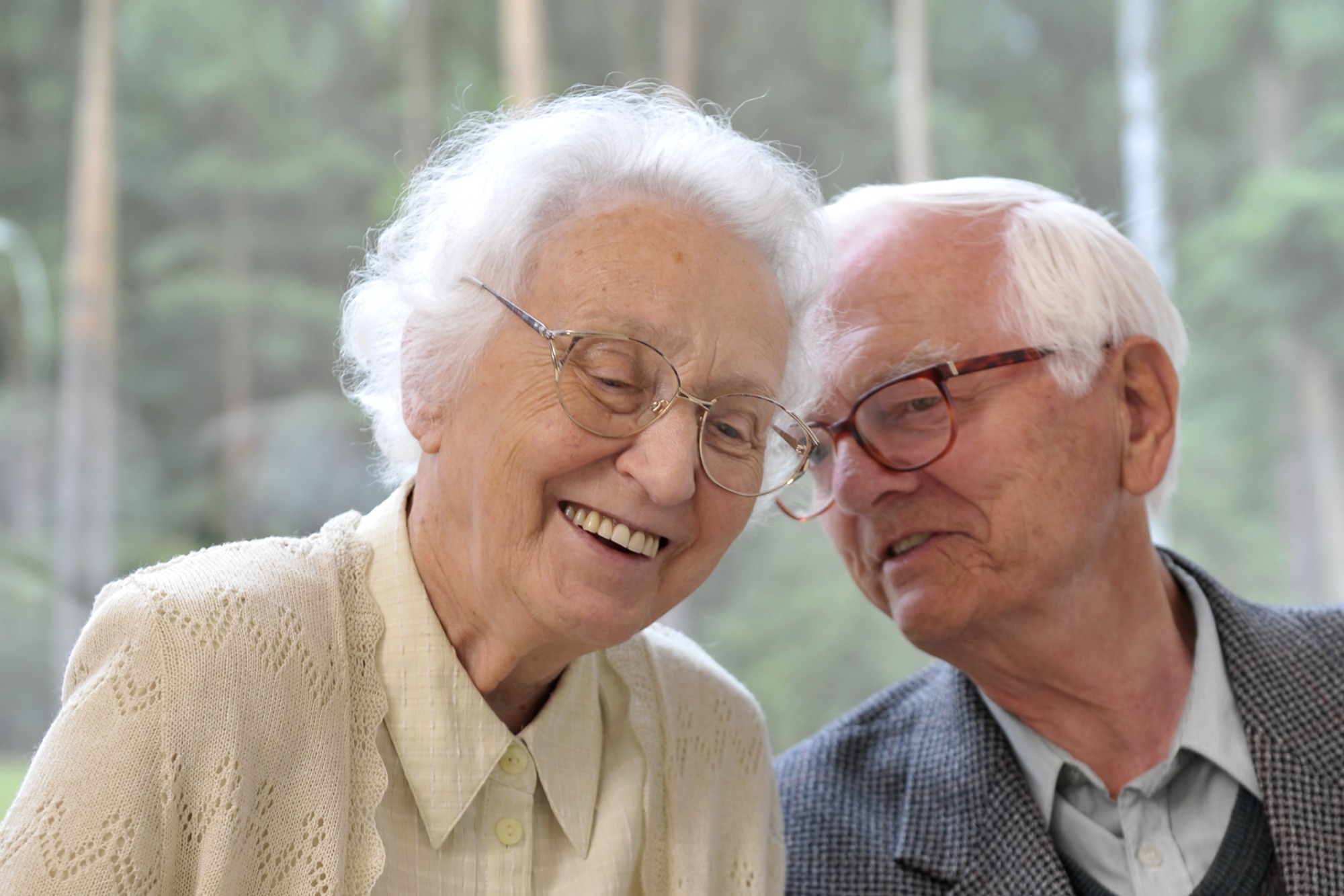 Zwei alte Menschen mit Brille sitzen fröhlich nebeneinander.